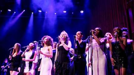 A group of women singing on stage

AI-generated content may be incorrect.